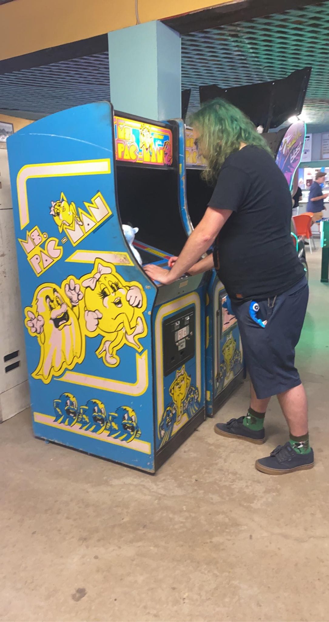 A man with green hair plays a Ms. Pacman arcade game, Photo 1